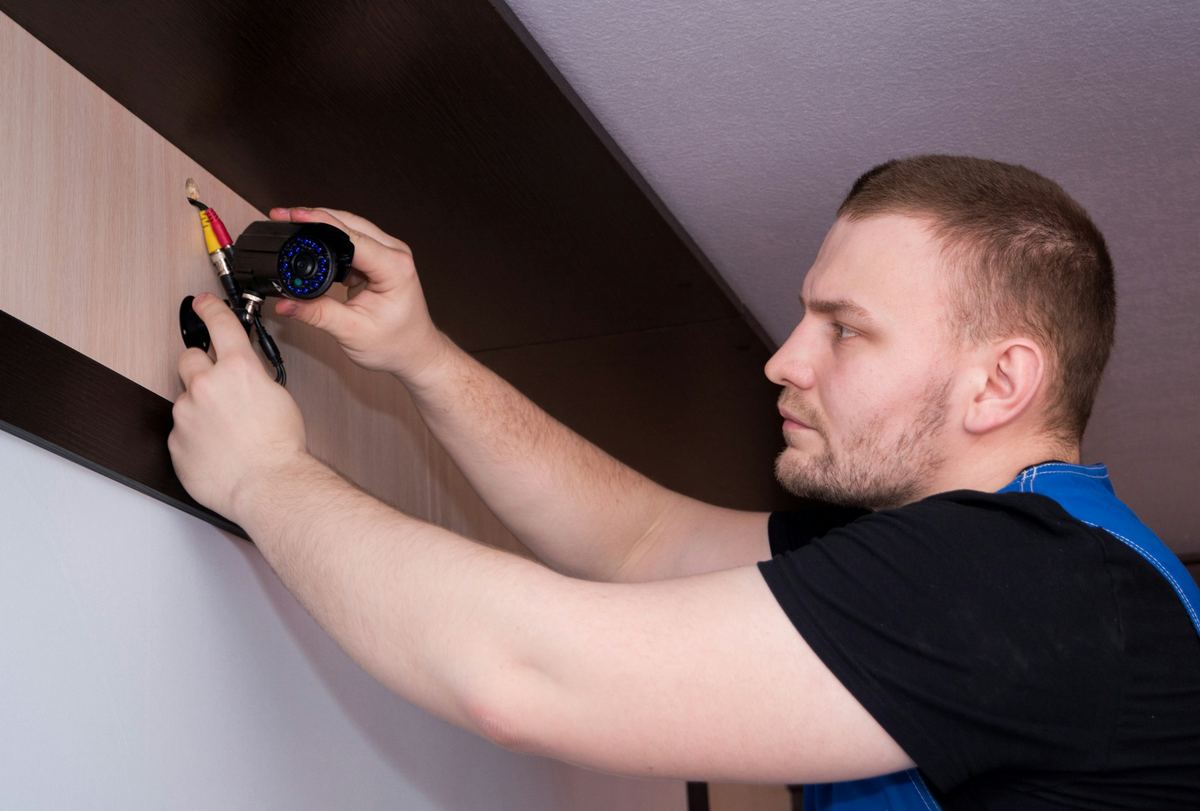 Een vakman monteert een camera tegen een plafond