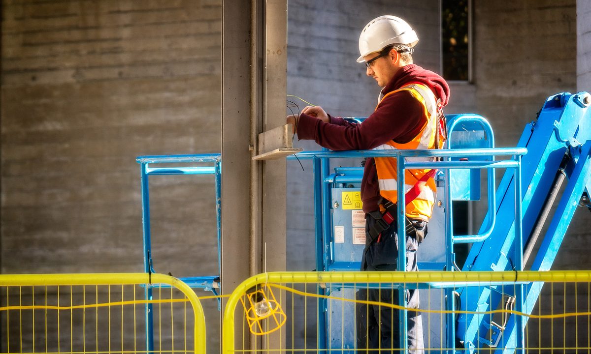 Een elektricien met helm op een hoogwerker sluit draden aan op een bouwplaats